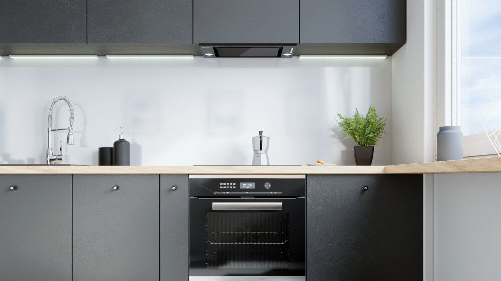 OKAP GLOBALO DESOLERO 60.3 Ciemna kuchnia z okapem do zabudowy umieszczonym pod górnymi szafkami na tle ściany z kamiennych płytek, z piekarnikiem w zabudowie poniżej, deską do krojenia, relingiem z akcesoriami i doniczką przy oknie