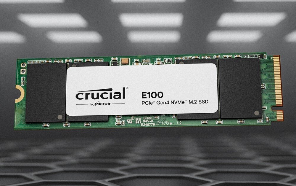 Dysk CRUCIAL E100 Dysk SSD w formacie M.2 z oznaczeniem 'E100' leżący na tle przypominającym siatkę z podświetleniem, opis