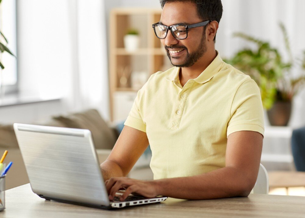 Dysk CRUCIAL E100 Mężczyzna w żółtej koszulce siedzący przy biurku i pracujący na laptopie w jasnym pomieszczeniu, prędkość, odczyt, zapis, interfejs