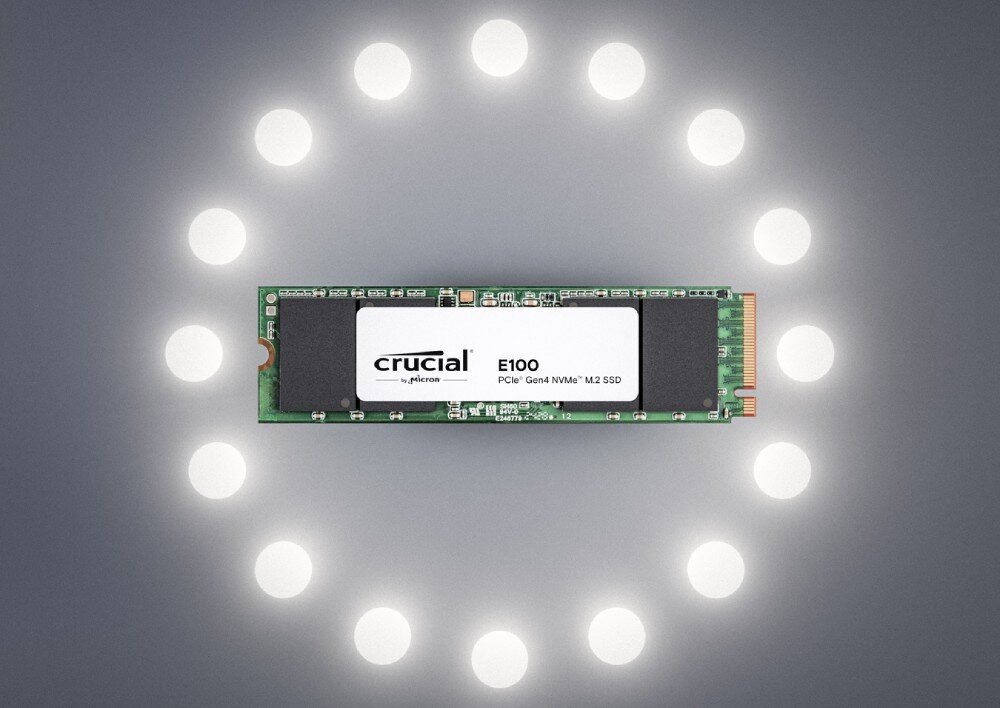 Dysk CRUCIAL E100 Dysk SSD M.2 z napisem 'E100' otoczony okręgiem z jasnych punktów świetlnych na ciemnym tle, pojemność, testy