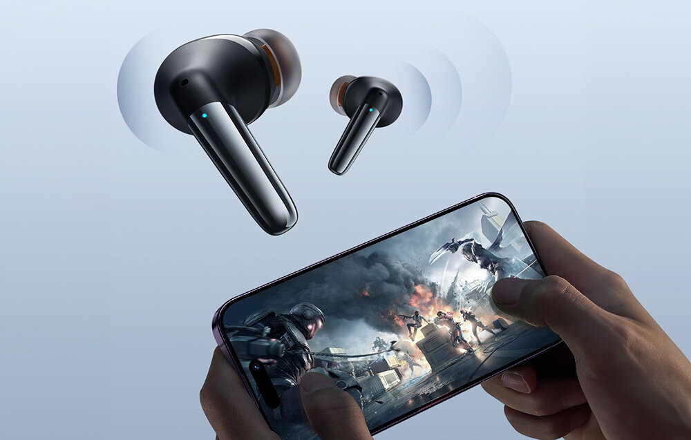 Na obrazie widoczne są czarne słuchawki bezprzewodowe oraz dłonie trzymające smartfon z wyświetloną grą akcji. Słuchawki mają nowoczesny design z niebieskim akcentem świetlnym.