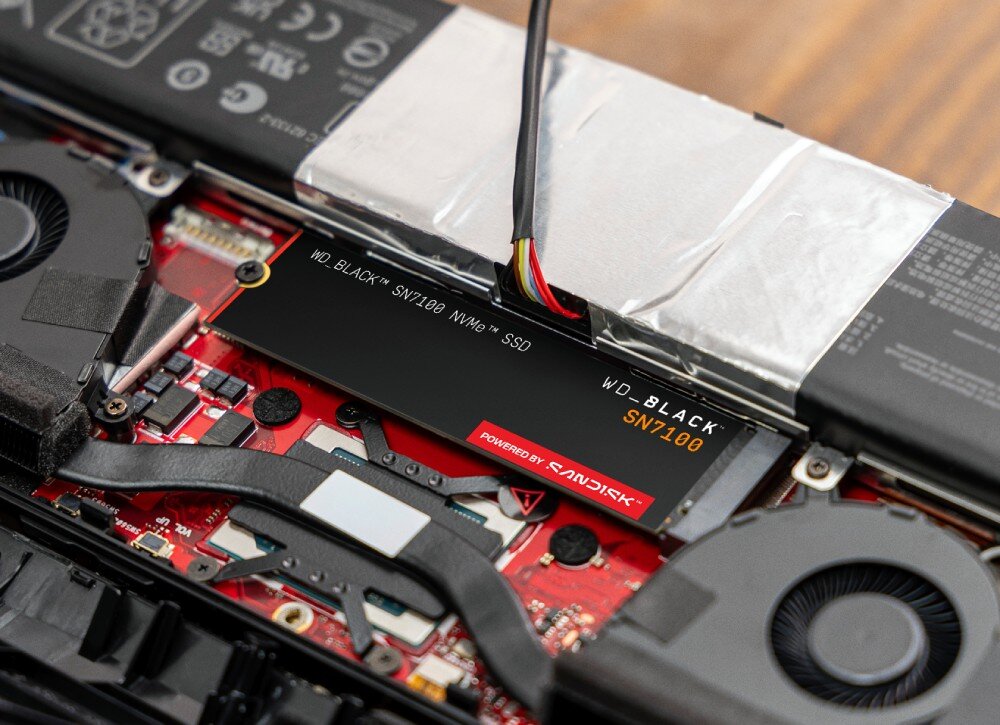 Dysk SANDISK WD Black SN7100 Podłużny dysk SSD M.2 zamontowany wewnątrz otwartej obudowy urządzenia elektronicznego pomiędzy baterią a wentylatorem chłodzącym, wydajność, efektywność, wytrzymałość