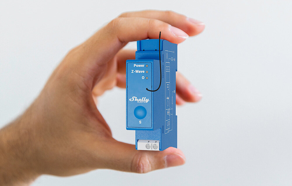 Przekaźnik SHELLY Qubino Z-Wave Pro 1, zasilanie, sterowanie, elektryka, napięcie, dłoń trzyma przekaźnik i eksponuje go frontem prawo skos