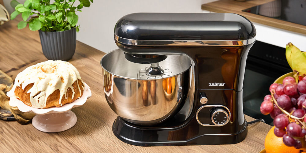 Robot planetarny ZELMER ZKR1355 1200W czarny robot stoi na blacie pokrętło srebrna misa srebrne elementy obok stoi babka z polewą planetarny ruch mieszania odwzorowanie trajektorii Ziemi wokół Słońca mieszadła obracają się jednocześnie wokół własnej osi i wewnątrz misy równomierne łączenie składników jednolita, puszysta i napowietrzona masa precyzja efektywność mieszania optymalna konsystencja 