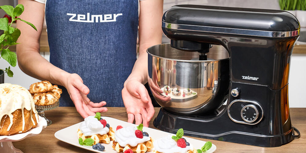 Robot planetarny ZELMER ZKR1355 1200W czarny robot stojący na blacie srebrna misa pokrętło srebrne elementy ręce ustawiające talerz ze słodkimi wypiekami ze śmietaną i owocami moc 1200 W wydajny pomocnik w kuchni duża moc ciężkie gęste masy długotrwałe mieszanie stała prędkość efektywność siła działania intensywne gotowanie  