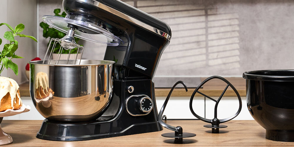 Robot planetarny ZELMER ZKR1355 1200W czarny robot na blacie srebrna misa otwarta pozycja zamontowana końcówka i osłona obok stoją czarne końcówki i widoczny jest kawałek czarnej misy różne końcówki do mieszania hak do zagniatania ciasta przygotowanie chleba ciasta drożdżowego i makaronu końcówka do ubijania ubicie bitej śmietany mieszadło kruche ciasto tłuczone ziemniaki hak do zagniatania i mieszadło pokryte teflonem bezpieczne mycie w zmywarce 
