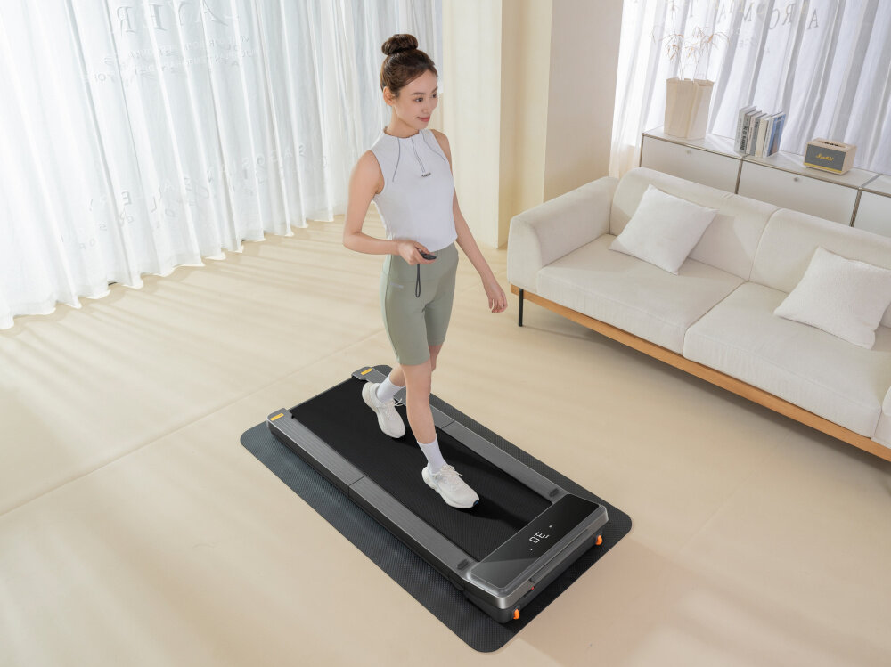 Bieżnia elektryczna KINGSMITH Z3 WalkingPad 735W 6km-h kobieta chodzi na bieżni w pokoju z pilotem w ręku składana prędkość do 10 km/h wytrzymała konstrukcja do spacerów intensywnych marszów do biegów