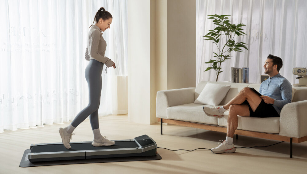 Bieżnia elektryczna KINGSMITH Z3 WalkingPad 735W 6km-h kobieta na bieżni kieruje pilot w stronę bieżni wyświetlacz LED Sterowanie pilot zdalnego sterowania ustawienia prędkości personalizacja treningu