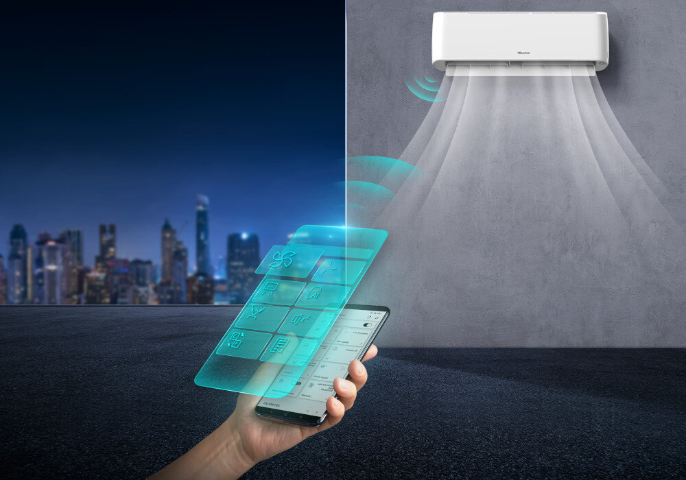 Na obrazie widoczny jest klimatyzator zamontowany na ścianie, z którego wydobywa się strumień powietrza. Przed nim znajduje się ręka trzymająca smartfon z wyświetlonym interfejsem aplikacji do sterowania klimatyzatorem.