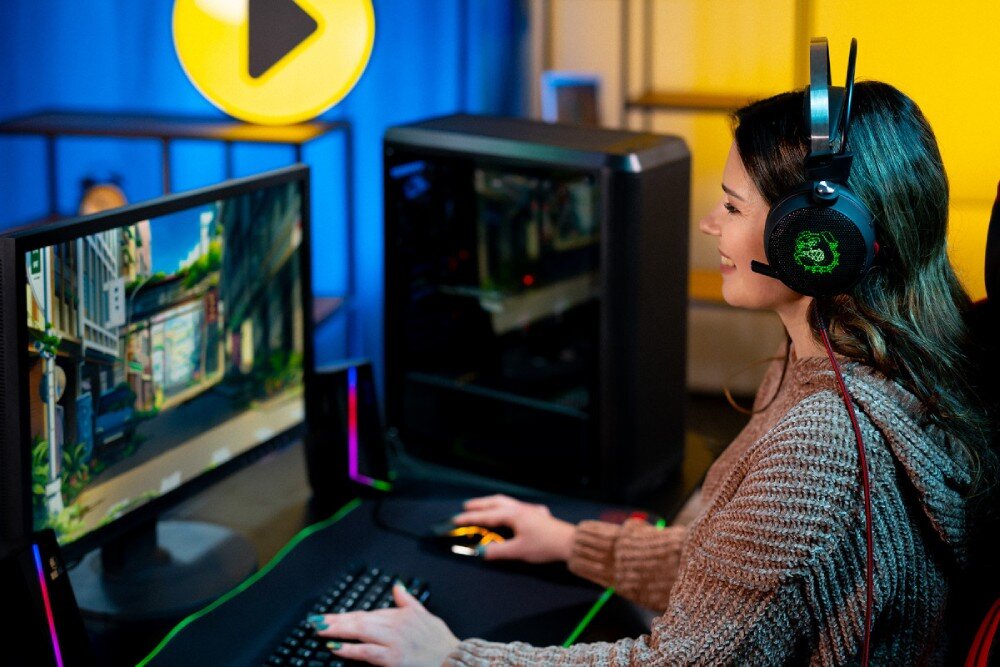 Komputer MAD DOG GeForce RTX4060 PurePC Edition 3 Widok od boku, kobieta w słuchawkach gamingowych siedząca przy biurku grająca w grę, w tle komputer wygląd opis