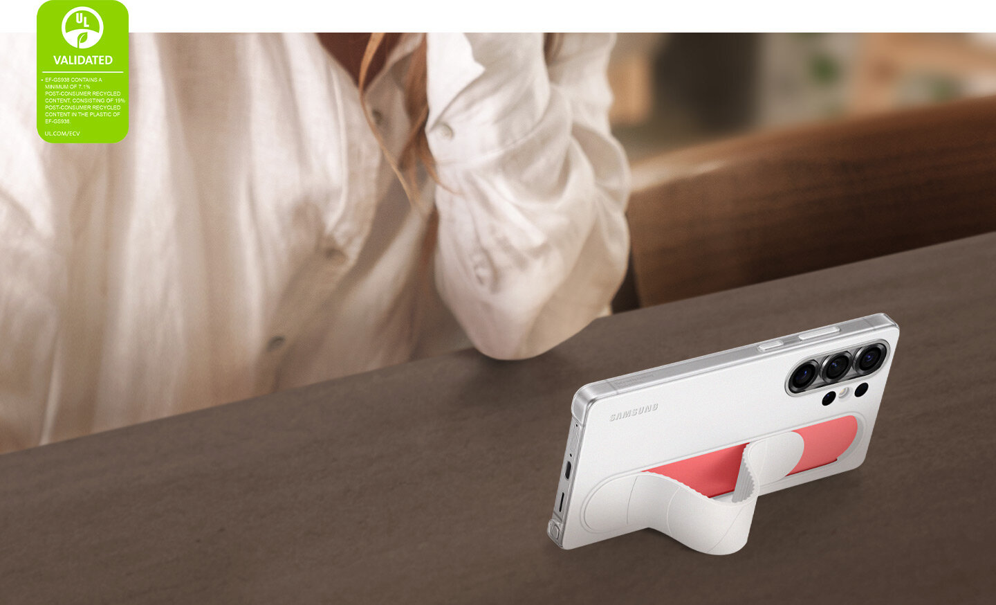 Galaxy S25 Ultra, z założonym białym etui Standing Grip Case, stoi pod kątem. Jest używany do oglądania filmów w trybie poziomym. W lewym rogu widoczny jest znak walidacji ochrony środowiska UL Environmental Claim Validation Mark z napisem 'EF-GS938 ZAWIERA MINIMUM 7,1% MATERIAŁU POCHODZĄCEGO Z RECYKLINGU POKONSUMENCKIEGO, W TYM 19% MATERIAŁU POCHODZĄCEGO Z RECYKLINGU POKONSUMENCKIEGO W PLASTIKU EF-GS938. UL.COM/ECV'.