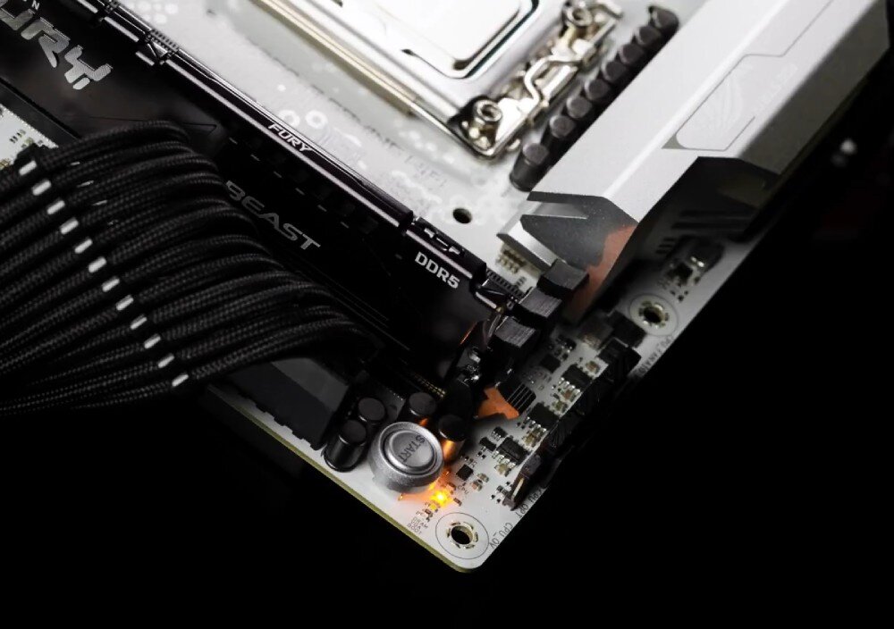 Płyta główna ASUS ROG Strix B860-G Gaming WiFi Zbliżenie na narożnik płyty głównej z przyciskiem 'START', podświetloną diodą Q-LED i czarnymi przewodami zasilającymi obok modułów pamięci DDR5, ułatwienia montażu