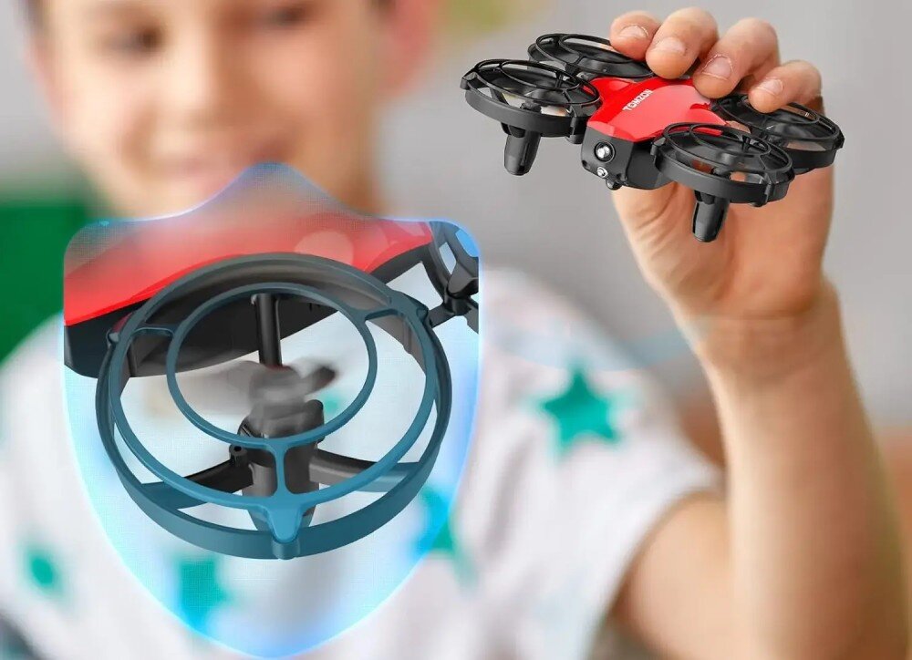 Dron EXTRALINK A24 Dłoń dziecka trzymająca mały dron z czerwonym korpusem, z widocznym zbliżeniem na kręcące się śmigło osłonięte grafiką błękitnej tarczy