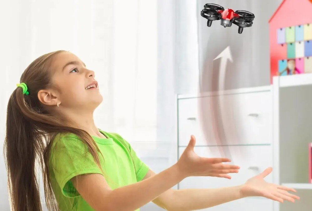 Dron EXTRALINK A24 Dziewczynka z uśmiechem patrzy w górę na unoszący się nad jej dłońmi mały dron, za którym widoczne są graficzne smugi wskazujące kierunek lotu do góry