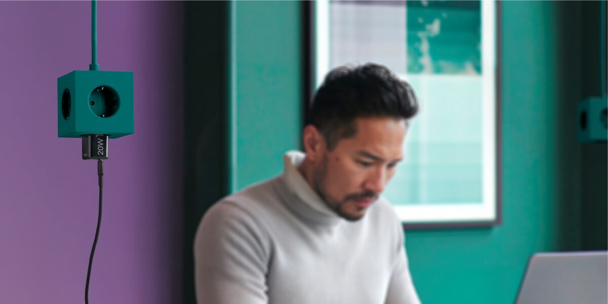 Kompaktowy ładowarka - ładowarka wpięta do przedłużacza w tle osoba pracująca przy komputerze