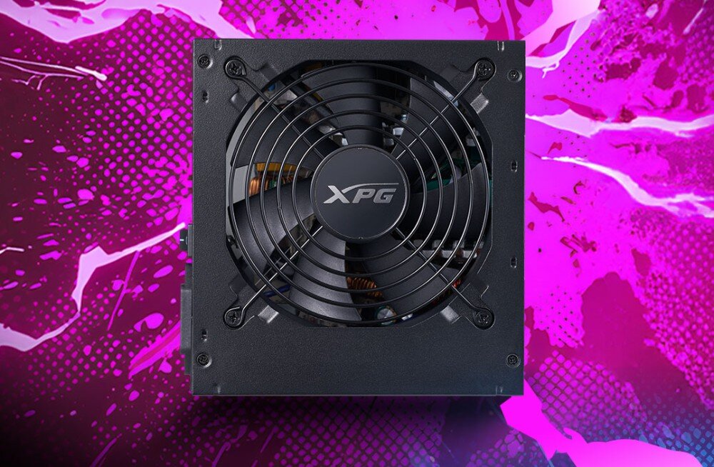 Zasilacz XPG PROBE Widok z góry na czarną obudowę zasilacza z centralnie umieszczonym wentylatorem pod okrągłym grillem na jaskrawym, różowo-fioletowym tle