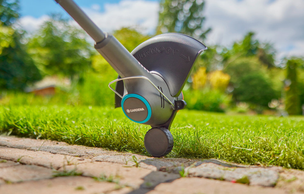 Podkaszarka akumulatorowa GARDENA EasyTrim 14704-20 zbliżenie na kółko w tle trawnik i rośliny specjalne kółko krawędziowe umożliwia prowadzenie po podłożu i uzyskanie równych, estetycznych linii cięcia chroni także żyłkę przed uszkodzeniem