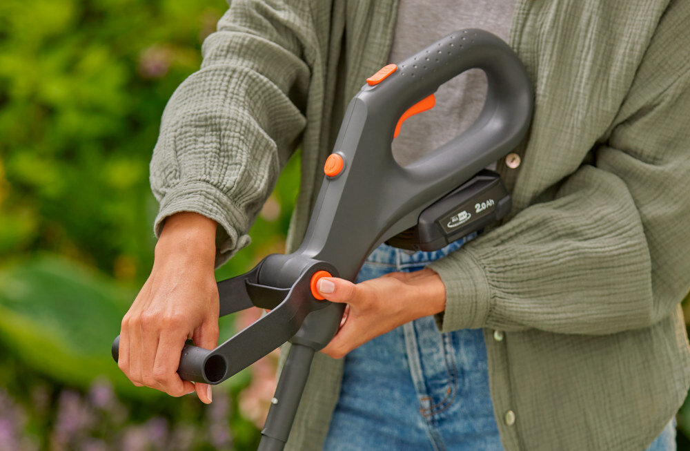 Podkaszarka akumulatorowa GARDENA EasyTrim 14704-20 osoba trzyma podkaszarkę w dłoniach reguluje uchwyt regulowany uchwyt dostosowanie pozycji chwytu do indywidualnych potrzeb zmniejsza obciążenie nadgarstków poprawia kontrolę nad urządzeniem
