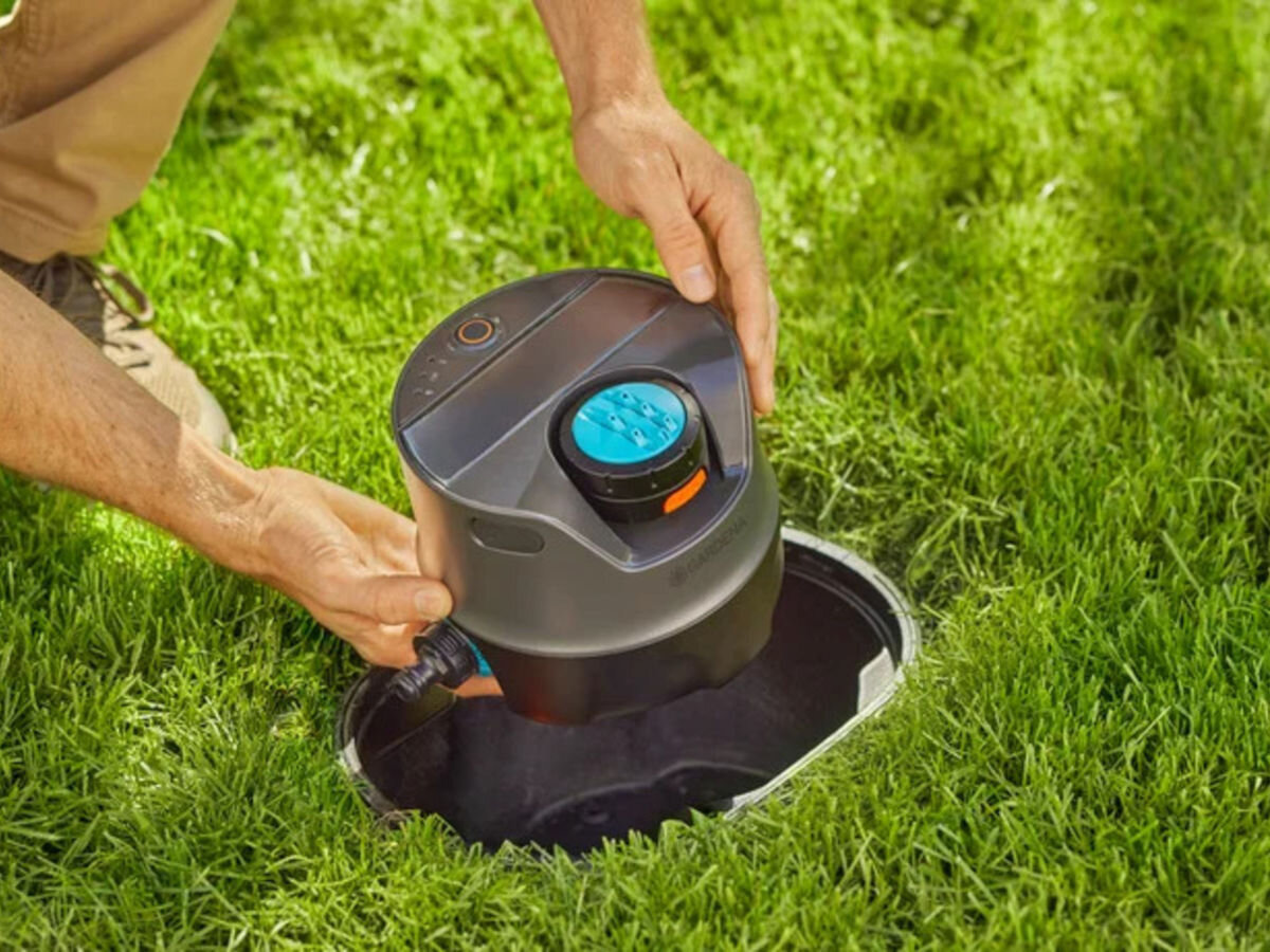 Skrzynka podziemna AquaPrecise GARDENA 16021-20, podziemne, ukryte, schowane, ogród, osoba trzyma zestaw nawadniający i wkłada go do skrzynki do ziemi