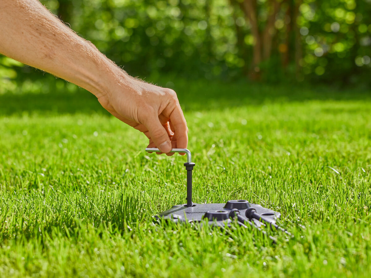 Skrzynka podziemna AquaPrecise GARDENA 16021-20, Plug&Play, AquaPrecise, nawadnianie, elementy, w tle ogród, dłoń wkręca śrubę do obudowy podziemnej skrzynki