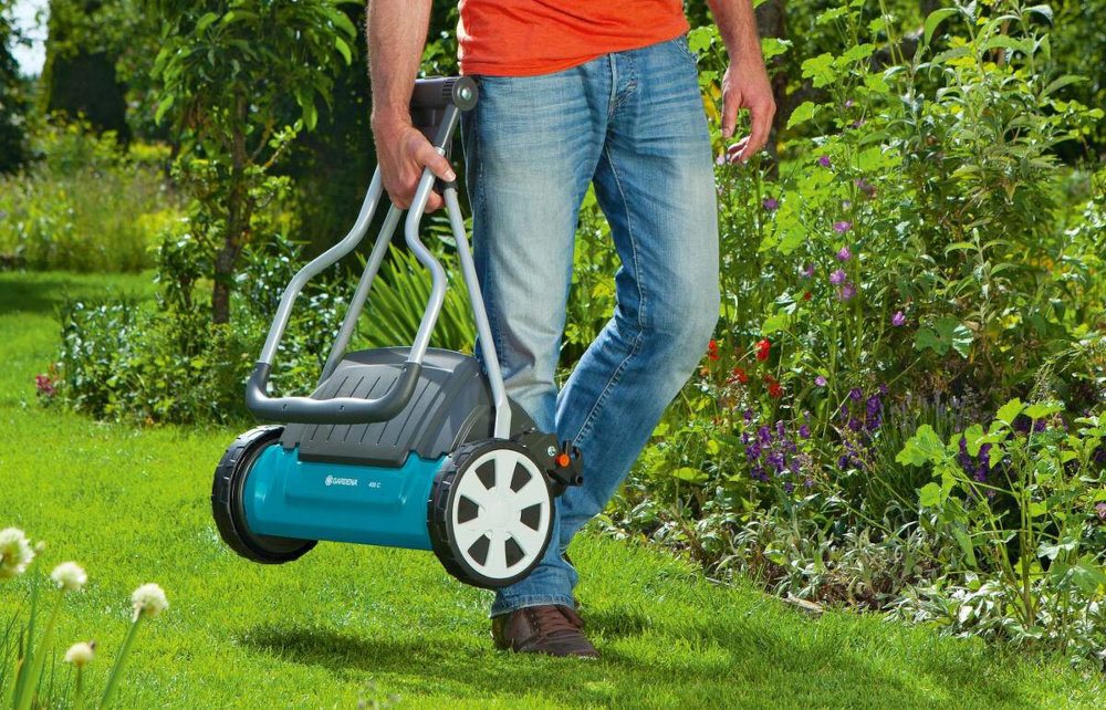 Kosiarka ręczna GARDENA Comfort 400 C regulacja 4-stopniowa 04022-20 ogród trawnik osoba niesie kosiarkę w dłoni w tle krzewy kwiaty do pielęgnacji małych trawników o powierzchni do 250 m² szerokość koszenia do 40 cm szybko i równomiernie przycina trawę mechanizm bębnowy działa bezdotykowo cicha płynna i precyzyjna pielęgnacja trawnika bez konieczności używania prądu