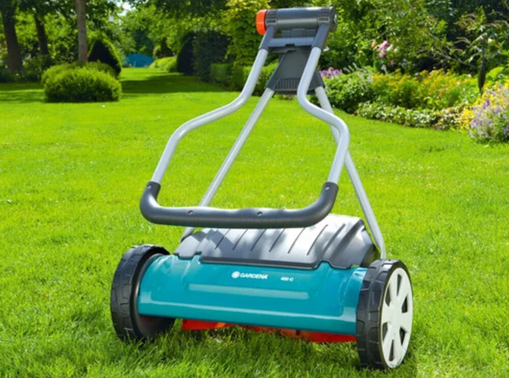 Kosiarka ręczna GARDENA Comfort 400 C regulacja 4-stopniowa 04022-20 ogród trawnik złożona kosiarka stoi na trawie w tle krzewy drzewa kwiaty nie wymaga paliwa i zasilania elektrycznego przyjazna dla środowiska i domowego budżetu cicha praca bez emisji spalin i hałasu hartowana stal wysokiej jakości materiały konstrukcyjne powłoka antyadhezyjna chroni cylinder przed korozją i zabrudzeniami