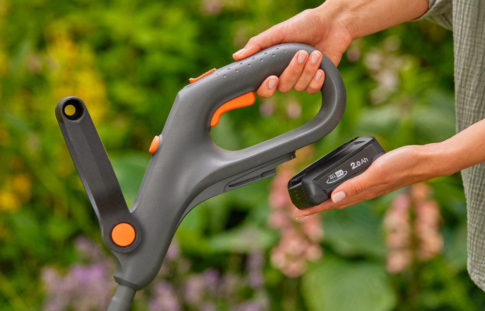 Podkaszarka akumulatorowa GARDENA EasyTrim 14704-55 zbliżenie na akumulator osoba trzyma podkaszarkę i akumulator w dłoniach zasilana jest akumulatorem 18 V o pojemności 2 Ah system POWER FOR ALL do 22 minut pracy na jednym ładowaniu pasuje również do innych narzędzi ogrodowych i domowych tej samej serii zaoszczędzić na zakupie