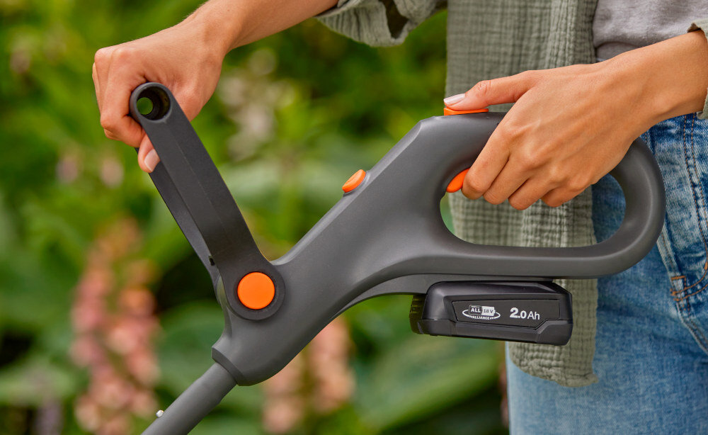 Podkaszarka akumulatorowa GARDENA EasyTrim 14704-55 osoba trzyma podkaszarkę w dłoniach przyciska palcem przycisk szybka i łatwa pielęgnacja ogrodu dwa tryby tryb przycinania tryb przycinania krawędzi zmiana za pomoc,ą przycisku uchwyt o dużym zasięgu