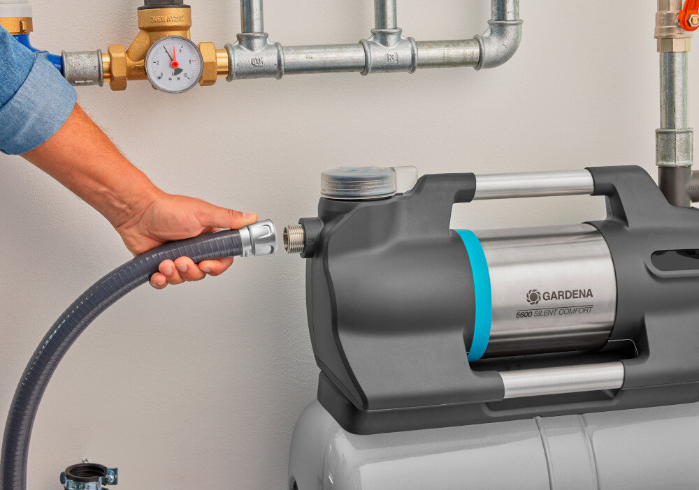 Wąż ssący GARDENA 9092-20 4 m pomieszczenie osoba podłącza wąż do pompy jasna ściana liczniki na ścianie wszechstronne urządzenie skuteczne zasysanie wody stabilne i szczelne połączenie uniwersalne zastosowanie