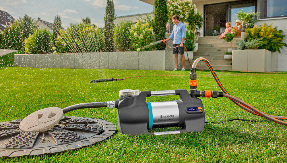 Wąż ssący GARDENA 9092-20 4 m ogród wąż umieszczony w studzience kanalizacyjnej pompuje wodę do pompy  w tle osoba podlewa trawnik dom spiralna budowa elastyczność odporność na załamania waga 1,5 kg konstrukcja minimalizuje ryzyko skręceń