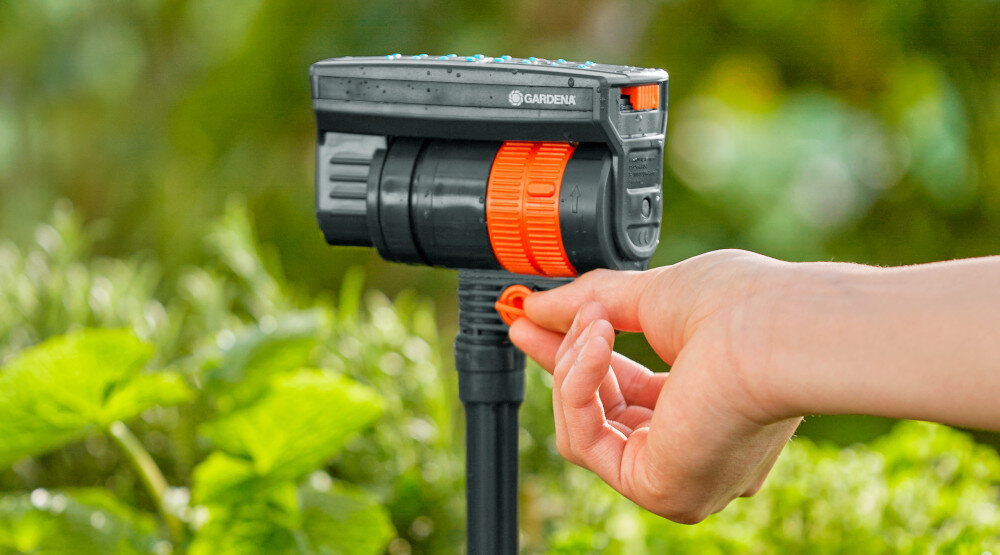 Zraszacz GARDENA Micro-Drip-System 13325-20 rozmyte zielone tło zraszacz osoba trzyma pokrętło w dłoniach zautomatyzowane podlewanie ograniczenie konieczności ręcznego nawadniania równomierne rozprowadzanie wody