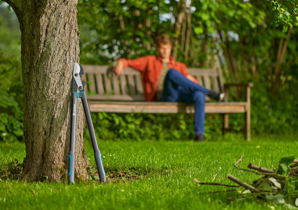 Nożyce do gałęzi GARDENA EnergyCut Pro L 12052-20 ogród drzewa nożyce oparte o pień drzewa w tle na ławce ogrodowej siedzi osoba wygodne przycinanie gałęzi precyzyjne cięcie