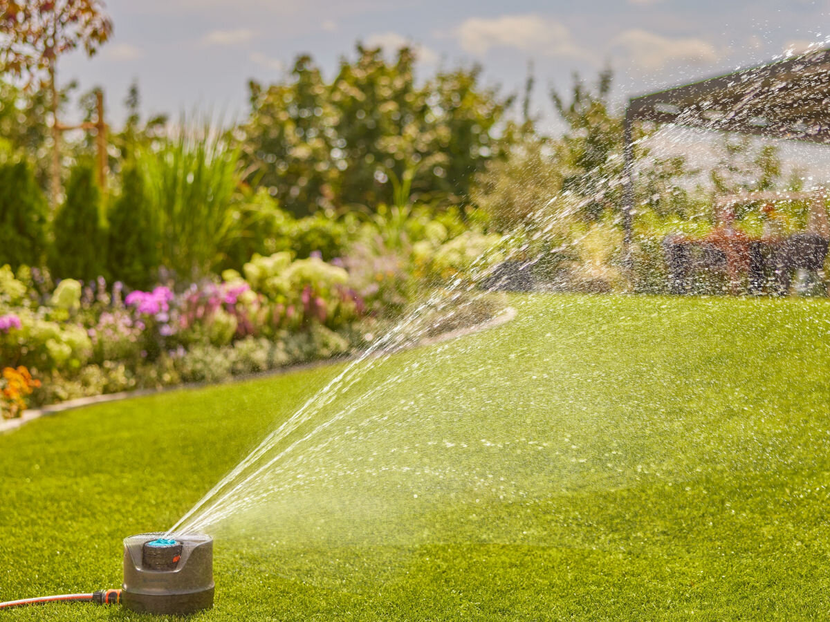 Zraszacz GARDENA AquaPrecise 16000-29, ogród, podlewanie, zraszacz, woda, w tle ogród i rabaty, na pierwszym planie zraszacz podlewa trawnik ogrodu