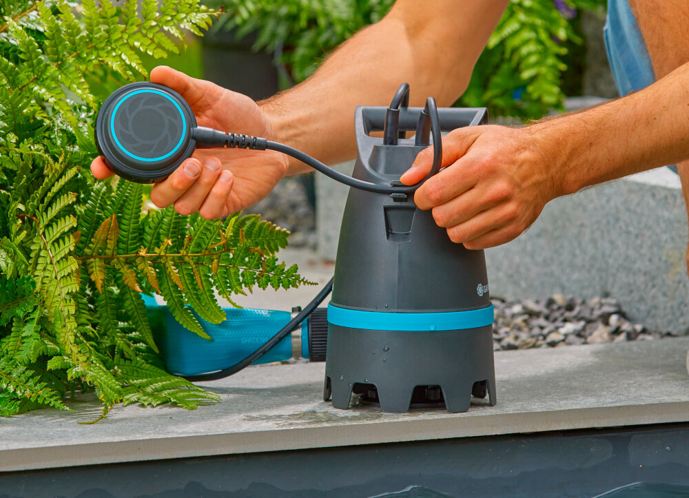 Pompa zanurzeniowa do wody brudnej GARDENA 10500 Basic 09008-47 elektryczna zbiornika z wodą w tle rośliny osoba trzyma pływak w dłoni praca na głębokości do maksymalnie 7 metrów regulowany wyłącznik pływakowy zabezpieczenie pompy przed pracą „na sucho” wał ze stali nierdzewnej wyłącznik termiczny zabezpiecza silnik przed przegrzaniem długa żywotność narzędzia trwałość