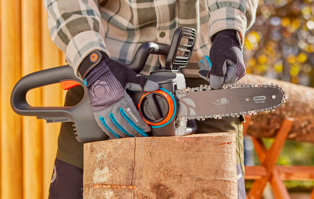 Piła akumulatorowa GARDENA PowerSaw 14790-55 osoba trzyma pokretło do regulacji w dłoniach w tle ogród łatwa obsługa wygodne użytkowanie napinanie łańcucha odbywa się bez użycia narzędzi praca z urządzeniem jest szybka i bezproblemowa