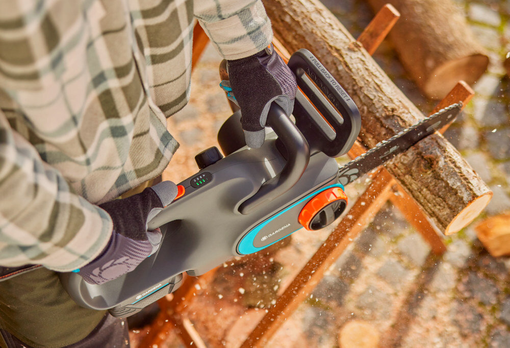 Piła akumulatorowa GARDENA PowerSaw 14790-55 osoba tnie kłodę drewna widok z góry bezpieczeństwo użytkownika wbudowany hamulec łańcucha zaczep zapobiegają przypadkowemu zerwaniu łańcucha
