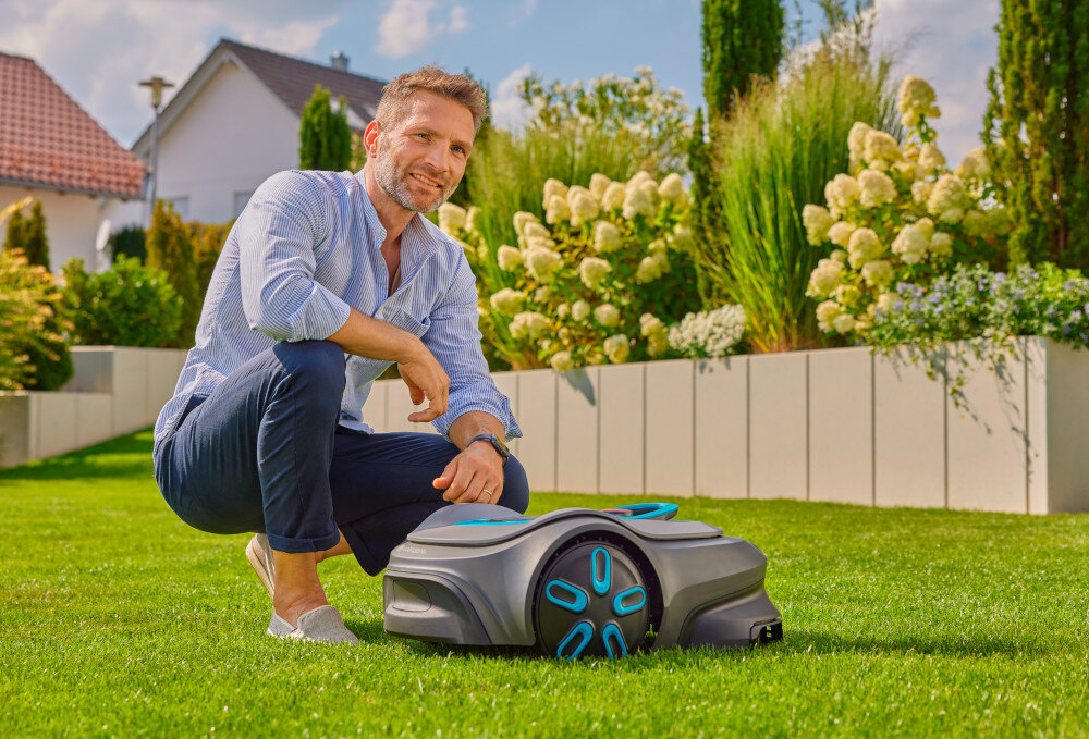 Robot koszący GARDENA Sielno Max 1500 19903-32 robot stoi na trawie obok kuca osoba dbanie o trawnik bez wysiłku na średnich i większych ogrodach o powierzchni do 1500 m² automatyczna praca cichy energooszczędna technologia