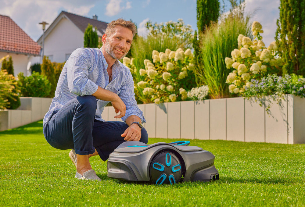 Robot koszący GARDENA Sileno Max 800 19901-32 robot stoi na trawie obok kuca osoba dbanie o trawnik bez wysiłku na średnich i większych ogrodach o powierzchni do 800 m² automatyczna praca cichy energooszczędna technologia
