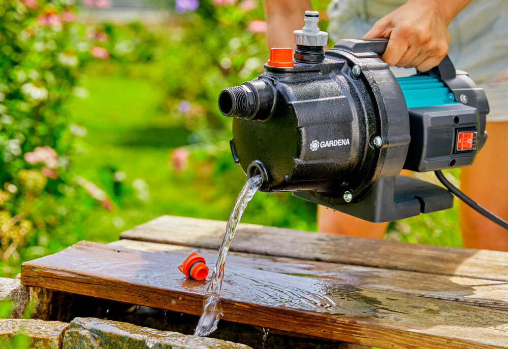 Pompa ogrodowa GARDENA 3700 Basic 9014-47 elektryczna osoba trzyma pompę za uchwyt opróżnia pompę z wody w tle rośliny praktyczny zintegrowany uchwyt ułatwia przenoszenie waga 8 kg kabel zasilający o długości 1,5 metra