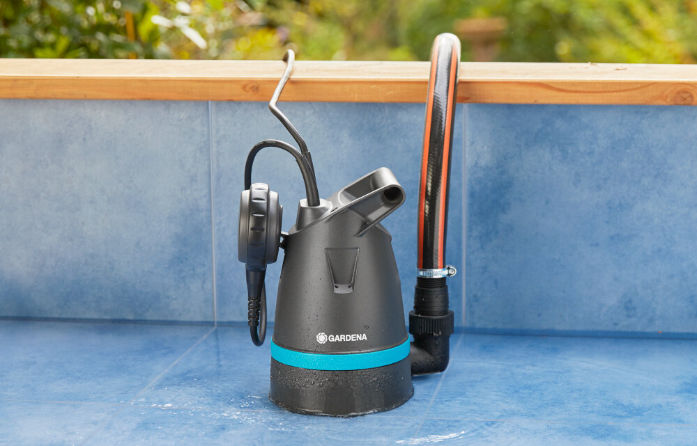Pompa do wody GARDENA 09001-47 elektryczna basen pompa umieszczona w basenie podłączony wąż w tle roślinność wygodne pompowanie wysoka skuteczność