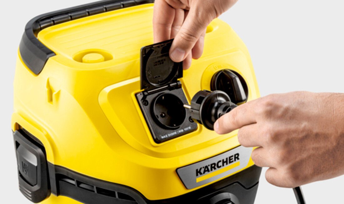 Osoba podłącza wtyczkę do gniazda w żółtym odkurzaczu marki KARCHER. Widoczne jest logo KARCHER na urządzeniu.