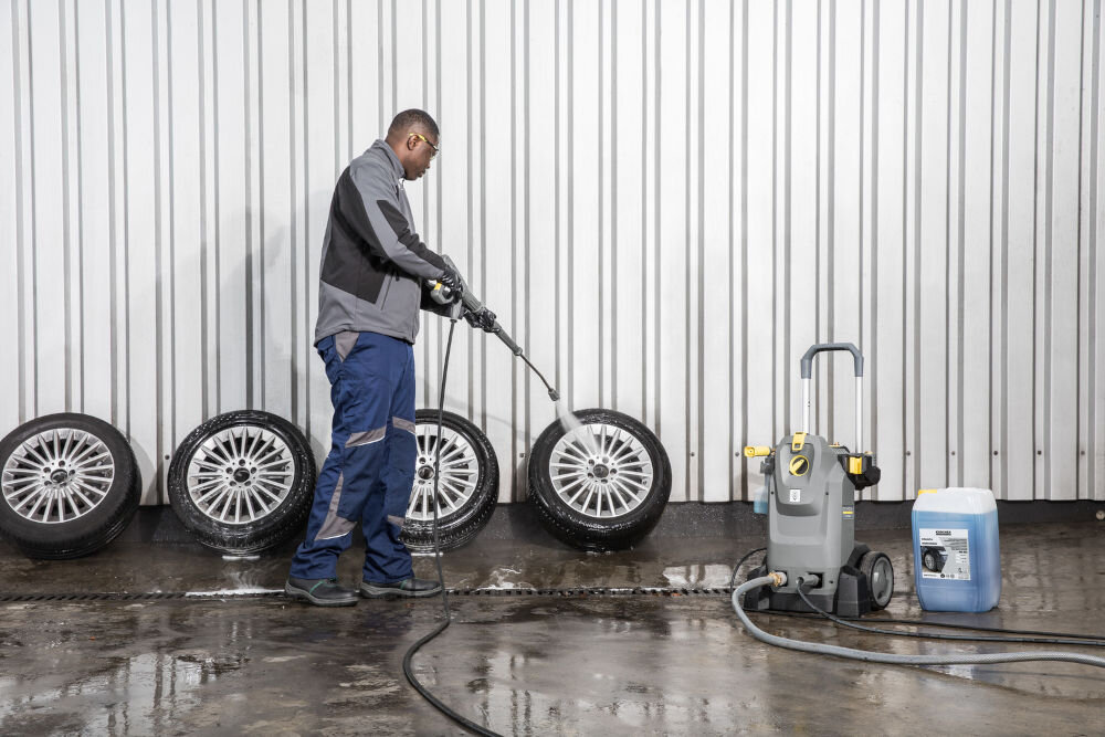 Myjka ciśnieniowa KARCHER HD 7/14-4M Plus 1.524-932.0 mężczyzna trzyma pistolet i strumieniem wody myje koła obok stoi myjka szary kolor żółte elementy ciągnący wąż efektywne czyszczenie
