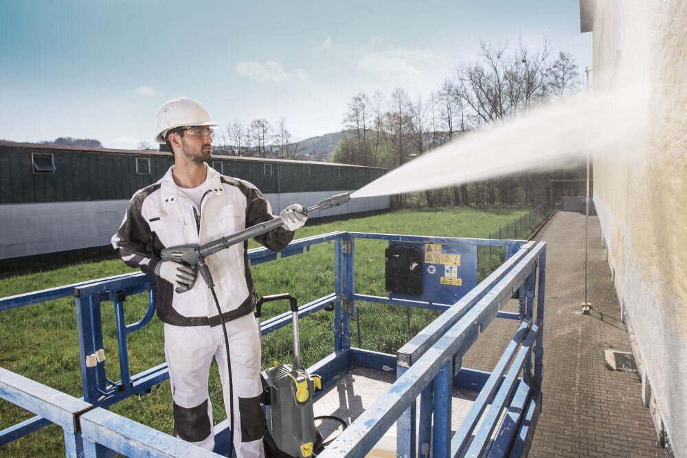 Myjka ciśnieniowa KARCHER HD 6/13 CX Plus 1.520-952.0 efektywne czyszczenie mężczyzna w roboczym ubraniu trzyma pistolet myje mur obok stoi szara myjka 