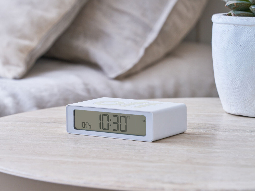 Budzik LEXON Flip Mini Biały, Budzik LEXON Flip Mini budzik w dłoni poranek alarm budzenie wybudzanie, Dłoń ustawiająca biały budzik z napisem „on”.