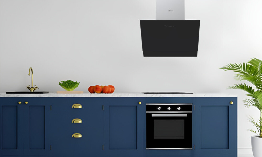 OKAP MIDEA MH60A4300B-ES Zdjęcie ukazuje kuchnię z granatowymi szafkami oraz czarnym okapem zamontowanym nad płytą grzewczą. Blat zdobią owoce i świeże warzywa klasa energetyczna A oszczędność wysoka Wydajność