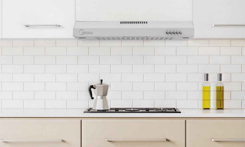 OKAP MIDEA MH60F17EM21WB Na zdjęciu widać biały okap kuchenny zamontowany nad płytą gazową. Przed nim stoi dzbanek do parzenia kawy oraz dwie butelki z oliwą, tworząc estetyczny, minimalistyczny wystrój kuchni