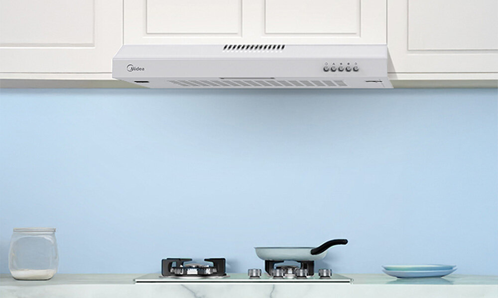 OKAP MIDEA MH60F17EM21WB Zdjęcie pokazuje biały okap kuchenny zamontowany pod szafką nad kuchenką gazową. Kuchnia utrzymana jest w jasnych, pastelowych kolorach, tworząc czysty, uporządkowany wygląd wydajna praca cicha smukła konstrukcja