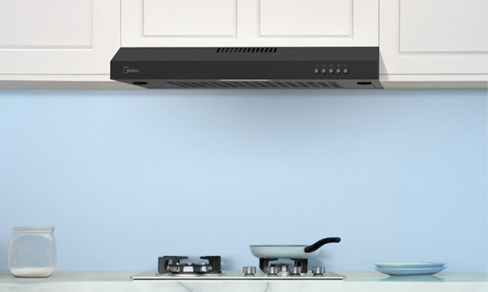 OKAP MIDEA MH60F17EM21BB Zdjęcie pokazuje czarny okap kuchenny zamontowany pod szafką nad kuchenką gazową. Kuchnia utrzymana jest w jasnych, pastelowych kolorach, tworząc czysty, uporządkowany wygląd wydajna praca cicha smukła konstrukcja