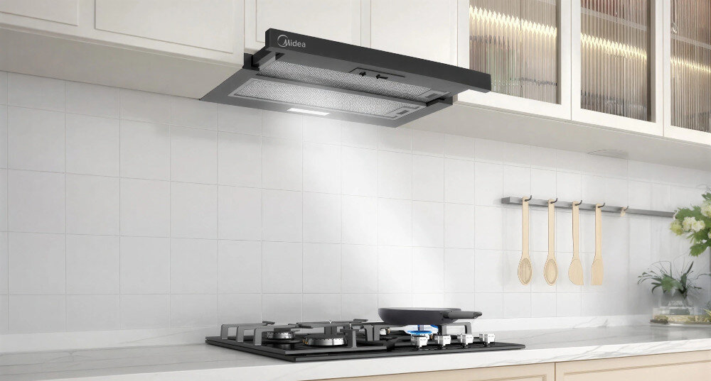 OKAP MIDEA MH60L07EM22BB Na zdjęciu widoczny jest okap kuchenny Midea zamontowany nad kuchenką gazową. Z urządzenia pada jasne światło oświetlające przestrzeń roboczą. design wygląd ukryta instalacja linia zabudowy