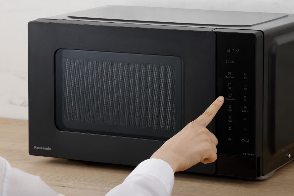 Czarna kuchenka mikrofalowa z panelem dotykowym, na którym widoczna jest dłoń wskazująca na przyciski. Na urządzeniu znajduje się logo \'Panasonic\'.